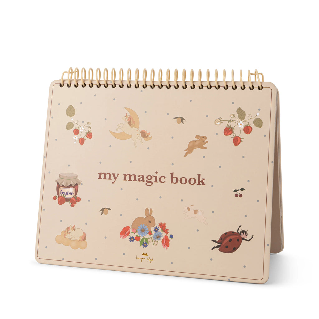 An off-white spiral-bound book titled "My Magic Water Book" stands upright. Its cover is adorned with whimsical illustrations including a bunny, a jar of honey, strawberries, flowers, a ladybug, and tiny gray dots scattered across the background. This magic water coloring book features reusable pages and comes with a refillable water brush pen.