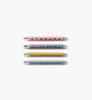 The Schoolhouse Gel Pen Set of 4 includes four vibrant pens featuring unique designs—red strawberries on white, red and blue dots on blue, yellow with ruler markings, and blue with a white checkerboard pattern. Each pen is equipped with a smooth 0.5 mm rollerball tip and is displayed horizontally against a white background.