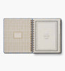 An open Schoolhouse 2027 17-Month Academic Hardcover Spiral Planner displays a gingham-patterned inside cover and a title page labeled “2026–2027 Monthly & Weekly Planner,” with tabbed sections visible along the right edge.