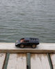 The Playforeer UFO Cannone Car in Black, inspired by 70's concept cars, sits on a wooden dock above the water with rippling waves in the background.