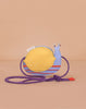 The Sticky Lemon Wallet Bag - Snail is a small crossbody for kids with a yellow shell, blue body, red stripes, purple strap with red tips, and is shown on a plain beige background.