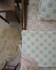 A cozy bedroom features a twin bed with the Organic Cotton Twin Size Blanket - Fleur, a patchwork pillow, a knitted pink throw, a wooden nightstand, and a fluffy cream rug on the floor.