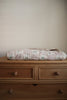 The Organic Cotton Twin Size Blanket - Fleur, featuring soft colors and a floral pattern, is neatly folded atop a light wood two-drawer dresser with round knobs, set against a plain beige wall.