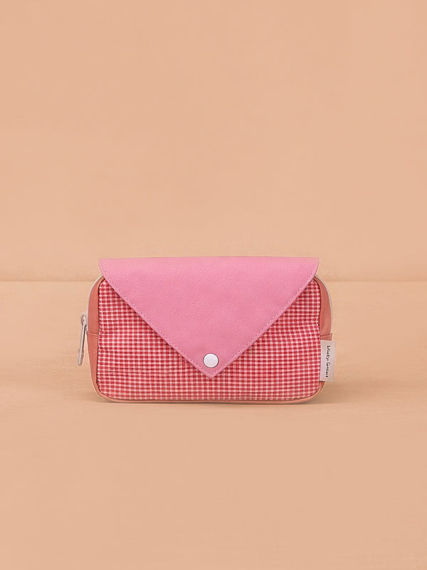 The Sticky Lemon Fanny Pack Small - Envelope - Rosebay Pink is a compact, rectangular bag with a pink flap and button closure, showcasing a red and white gingham front and waterproof recycled PET lining against a peach backdrop.