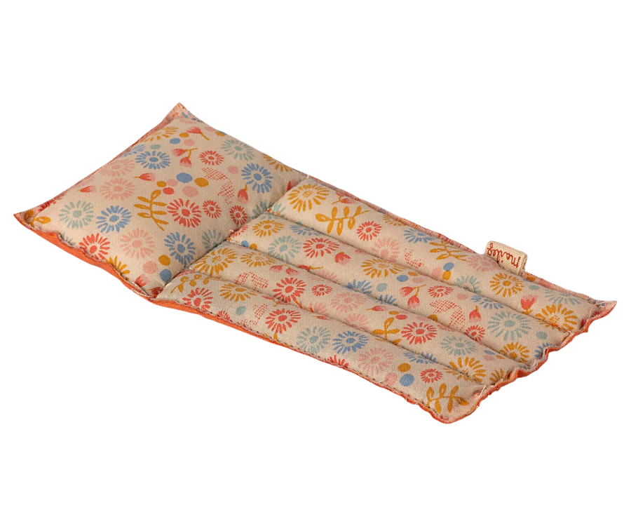 The Maileg Beach Float, Mouse - Flower is a rectangular heating pad adorned with a floral pattern, primarily featuring red, yellow, and blue flowers on a light background. This pad is segmented into three columns and made from durable raft-like fabric to ensure longevity. It also features a label on one edge.