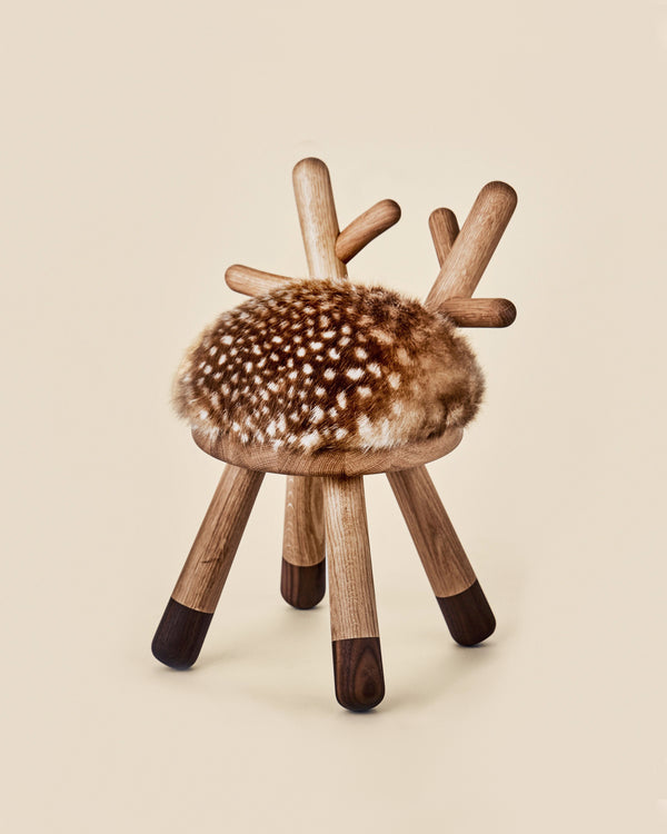 A unique Faux Bambi Chair with a round, faux fur-covered seat and wooden legs that branch out at the top in a tree-like manner, set against a soft beige background.