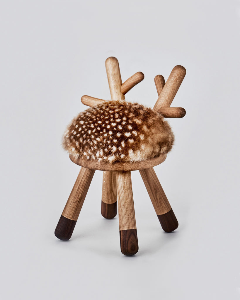 A unique Faux Bambi Chair with wooden legs and branches sticking out in different directions, topped with a faux fur, animal print cushion against a white background.