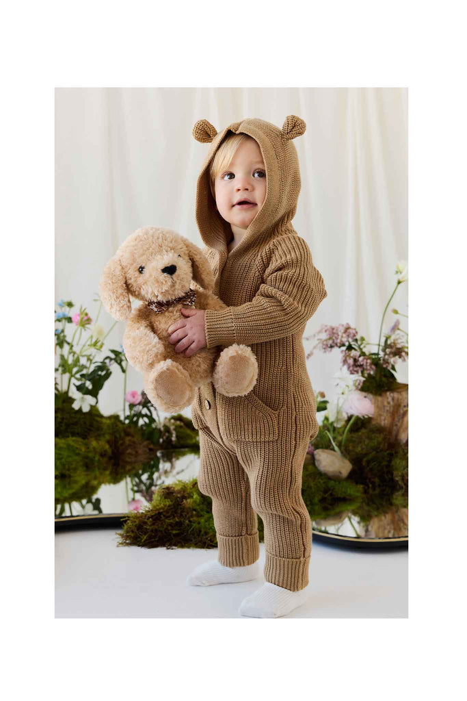 A toddler wearing a tan hooded knit romper with bear ears, cuddling with a Snuggle Bunnies - Honey the Puppy plush toy.
