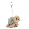 Introducing the Bukowski - Sandy Green Turtle Bag Charm: a plush sea turtle keychain featuring a beige head and legs, a soft green shell, and a metal clip attached by a string. Perfect as an adorable bag charm, it’s displayed against a white background.