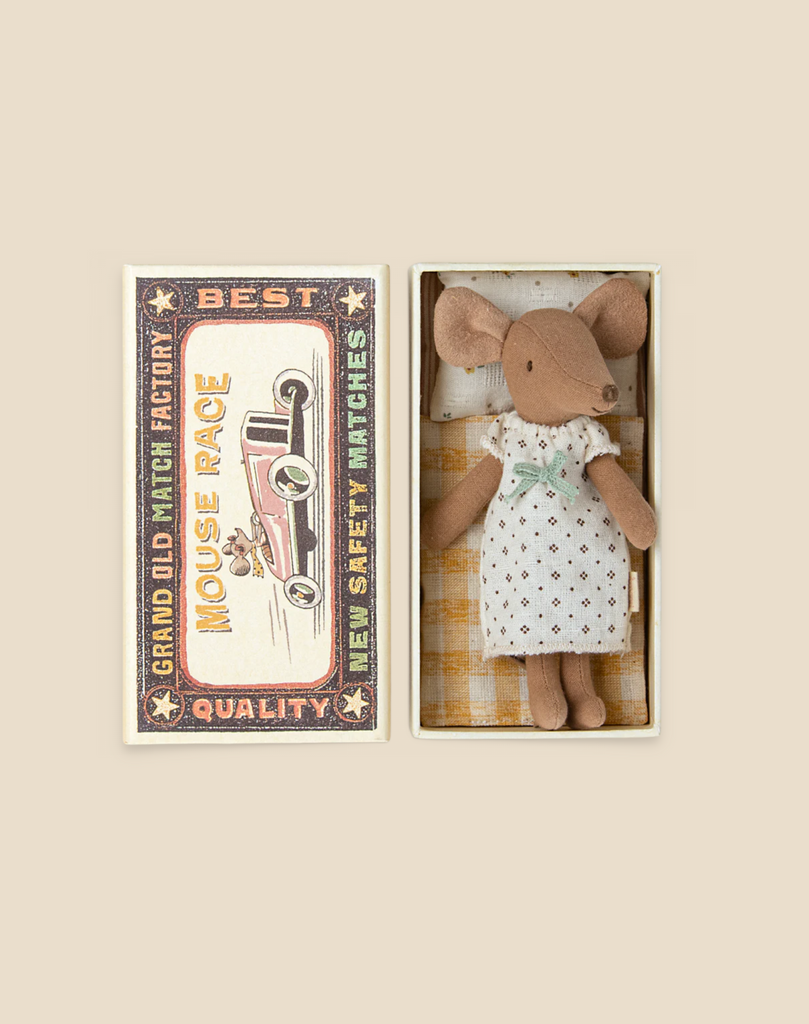 A vintage-style toy box containing a Maileg Big Sister Mouse in Box doll. The box has decorative text and graphics, and the mouse, dressed as a big sister in a dress with polka dots, is lying