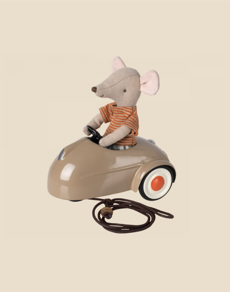 A Maileg Mouse Car - Light Brown dressed in an orange striped shirt driving a miniature vintage metal car with a pull string, against a light beige background.
