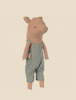 An adorable Maileg Pig In Overalls stands upright against a plain beige background. The pig is dressed in blue-green plaid overalls with an orange carrot peeking out of a pocket, adding to its charm.