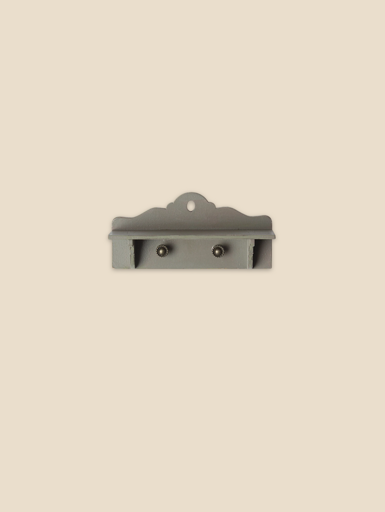 The Maile Bonus Room Bedroom Set features a small, decorative gray wall shelf with scalloped edges and two metal hooks, ideal for dollhouse or miniature bedroom display, shown mounted against a beige background.