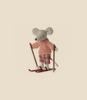 A small, cute stuffed toy mouse is shown standing on red skis, part of an adorable Maileg Christmas Winter Mouse With Ski Set, Big Sister. The mouse is dressed in a pink sweater and plaid pants and is holding ski poles in each hand. The background is a plain, light beige color.