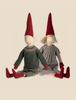 Two Maileg Christmas Pixy (Size 5) seated side by side, one wearing a green sweater and the other in a gray dress, both with long red hats and striped legs, crafted from exclusive materials.
