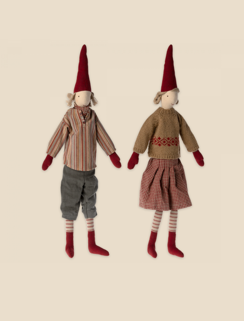 Two Maileg Christmas Pixy (Size 4) dolls, one dressed in a striped shirt and shorts, the other in a sweater and plaid skirt, both with red hats and socks, standing against a light background, designed as exclusive.