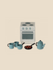 A miniature kitchen set featuring a white oven with silver knobs, a blue kettle, three blue mugs from Maileg Madam Blue’s Favorites, and a small frying pan with brown food items. The items are arranged on a light beige background, perfect for hosting the Mouse family's traditional Scandinavian treat.