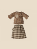 A set of doll clothes displayed on a light beige background. The outfit consists of a long-sleeved, brown patterned top with a delicate flower brooch, and a classic black and white checkered skirt reminiscent of Maileg Extra Clothing: Blouse And Skirt For Grandma Mouse.