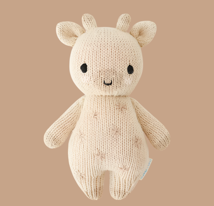 The Newborn Gift Set - Natural features a hand-knit baby giraffe plush made from natural Peruvian cotton yarn with black eyes, brown stitched spots, and short arms on a plain beige background.