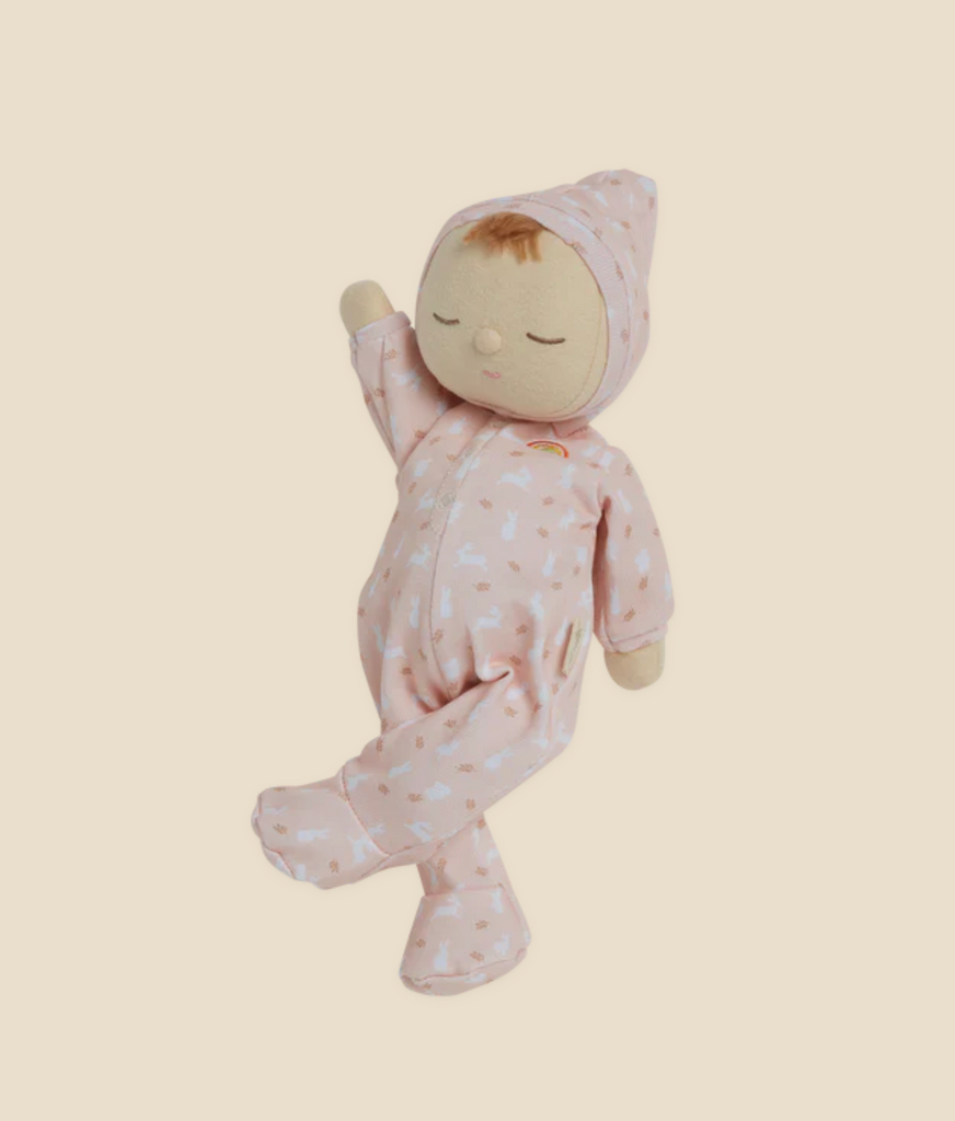 A soft Olli Ella x Odin Parker Dozy Dinkums - Blossom wearing a pink onesie crafted from 100% organic cotton with white patterns and a matching hood, floating against a light yellow background.