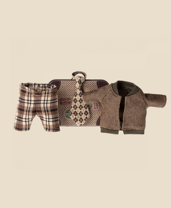 A neatly arranged display of Maileg Jacket, Pants And Tie In Suitcase, Grandpa Mouse. The set includes plaid shorts, a checkered tie, a brown cardigan with green trim, and a small metal suitcase adorned with travel stickers. The background is a solid beige color.