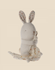 A beige stuffed rabbit sits upright, holding a soft polka dot blanket. This Maileg Lullaby Friends - Bunny - Nature (Plays Music) has ears with a floral pattern on the inner sides and small black eyes with minimal facial details, making it perfect for a baby gift box. The background is plain and light-colored.