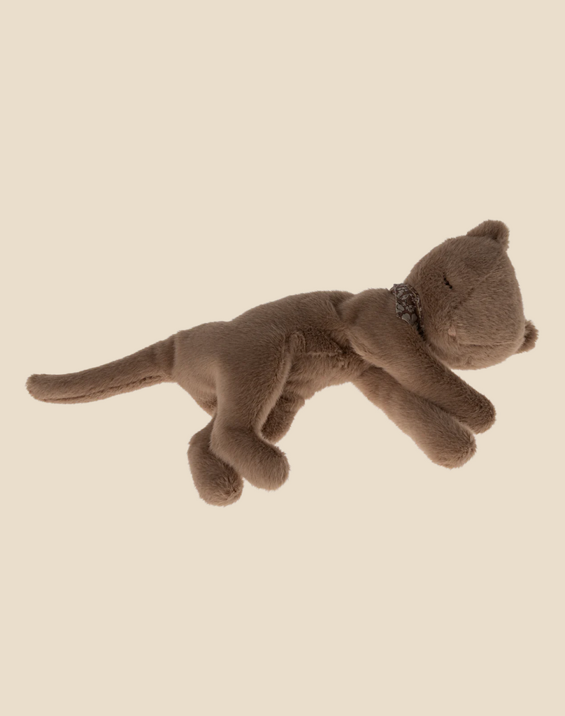 A Maileg Plush Kitten, Nougat (ships in approximately one week) lies on its side in a relaxed position, as if basking in a cosy basket, against a plain beige background. Part of the pet collection, this softest plush kitten features a long tail and sewn facial details, including closed eyes that suggest it is peacefully asleep.