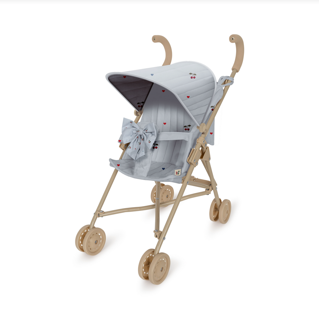 The Konges Sloejd Zoe Bow Doll Stroller - Cherry Blue boasts a stylish beige frame on four double twin wheels. It features a light gray padded canopy and seat adorned with a subtle heart pattern, along with coordinating bows on the front. The stroller is designed with curved beige handles and includes a convenient, foldable shade.