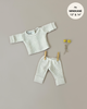 A Minikane Doll Clothing | Morgan Pajamas in Honeycomb Linen Knit set, perfect for Minikane Gordis dolls, is displayed on a neutral background. Two yellow flowers lie next to the pants, which are held up by wooden clothespins. A circular label in the top right corner reads "fits MINIKANE 13'' & 14''.