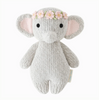 A Cuddle + Kind Baby Elephant, Blush Floral with large ears and black eyes. The elephant is wearing a pink flower crown on its head. Made from Peruvian cotton yarn, it has a hand-knit texture and a tag on its side, ensuring heirloom-quality charm.