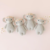 Four identical Cuddle + Kind Baby Elephant, Blush Floral plush toys, each adorned with a pink floral crown, are neatly lined up on a pale pink background. Small white flowers are scattered around them, enhancing the charming and whimsical scene crafted from heirloom-quality Peruvian cotton yarn.