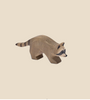 The Ostheimer Raccoon Running, a small hand-carved wooden figurine, is perfect for imaginative play. This raccoon features distinct facial markings and a bushy, striped tail. It stands on a plain brown surface against a solid light brown background, creating a minimalist and earthy aesthetic reminiscent of Ostheimer toys.