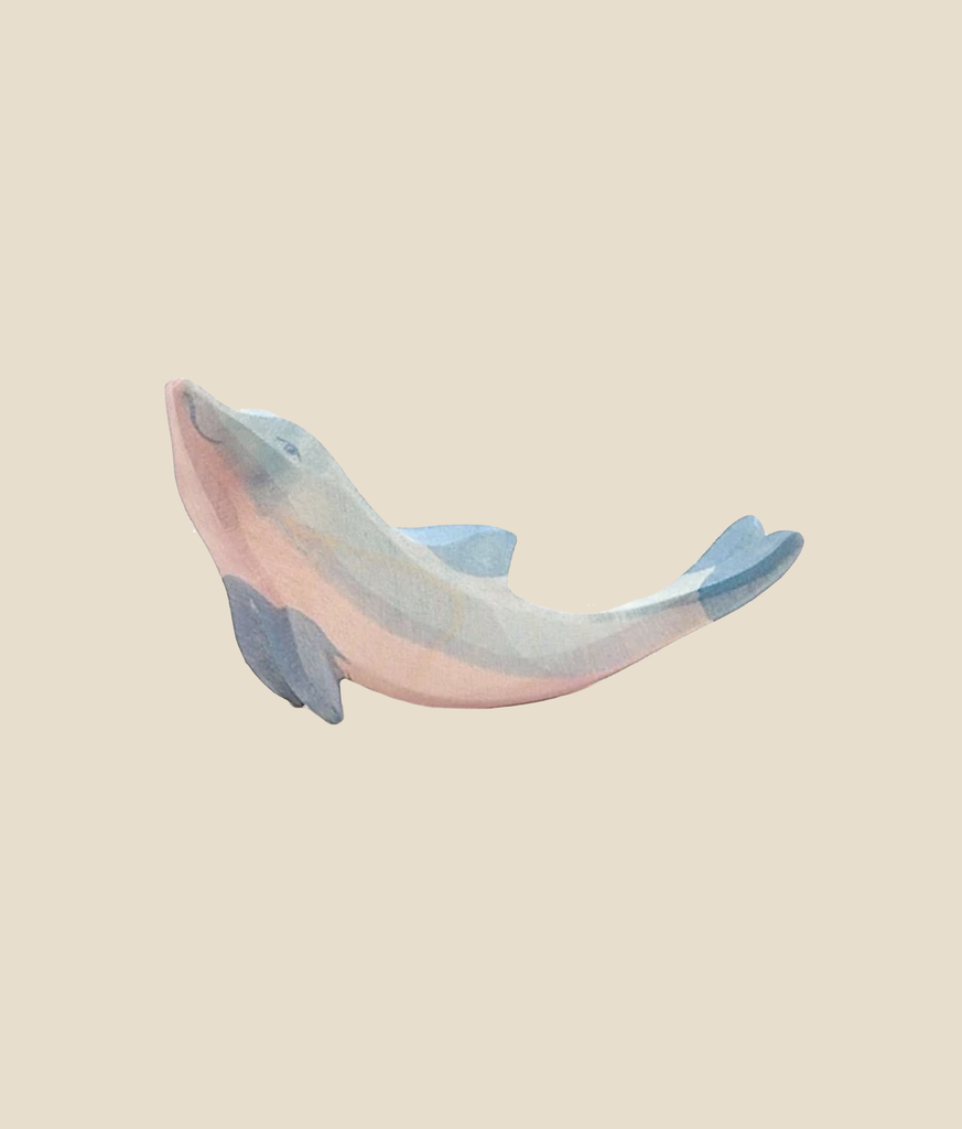 A small, smooth figurine resembling the Ostheimer Dolphin, Head High is displayed against a plain, warm beige background. Painted in shades of blue and pink, the dolphin is shown in a playful, leaping pose.