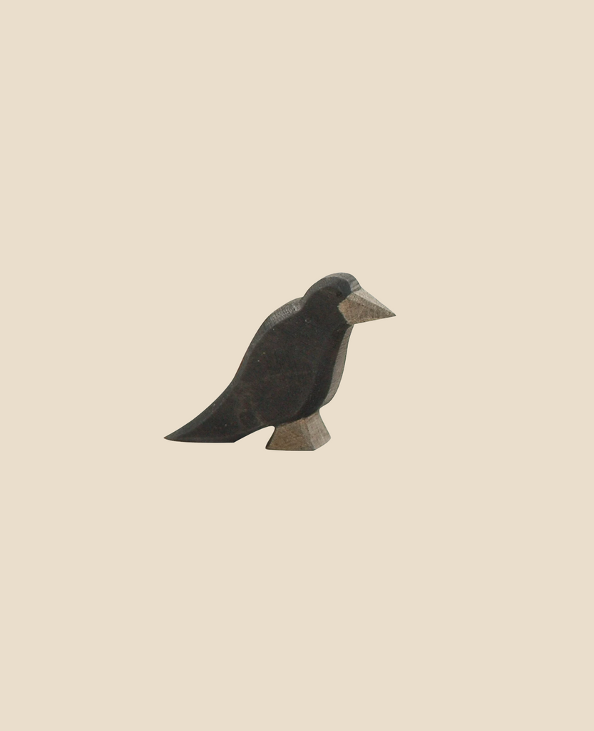 The Ostheimer Raven, a small and simplistic black bird figurine with a white beak and feet, stands against a plain beige background. This handcrafted wooden toy boasts a minimalist and artisan appearance, reminiscent of the beloved Ostheimer toys, and is crafted from sustainably sourced materials.