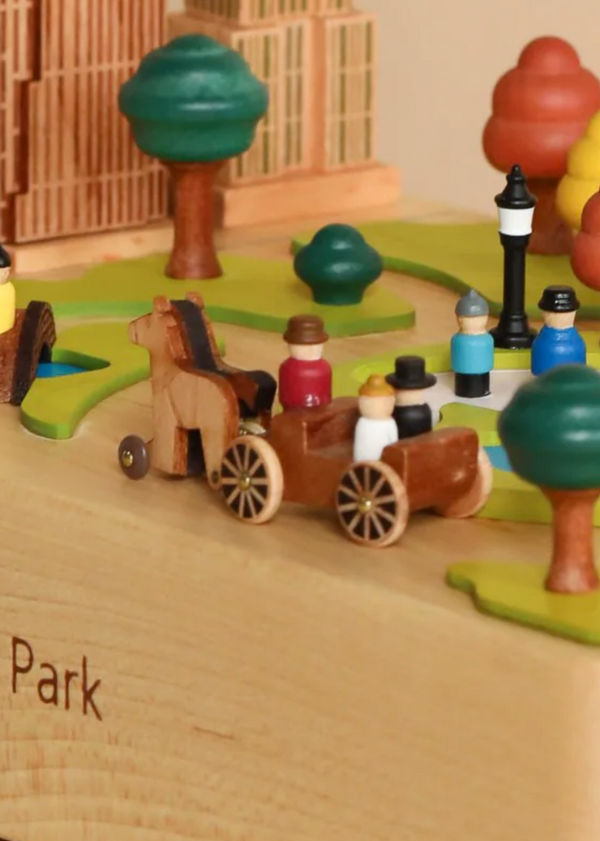 This delightful diorama features a charming horse-drawn carriage as the centerpiece, set among miniature trees and a streetlamp, all beautifully arranged in a wooden park scene. Colorful figures bring the display to life against the backdrop of detailed wooden structures. Elegantly engraved with "Park" on its base, this piece from the Carriage Replacement For Central Park Music Box collection invites contemplation and serves as an ideal ornamental addition.