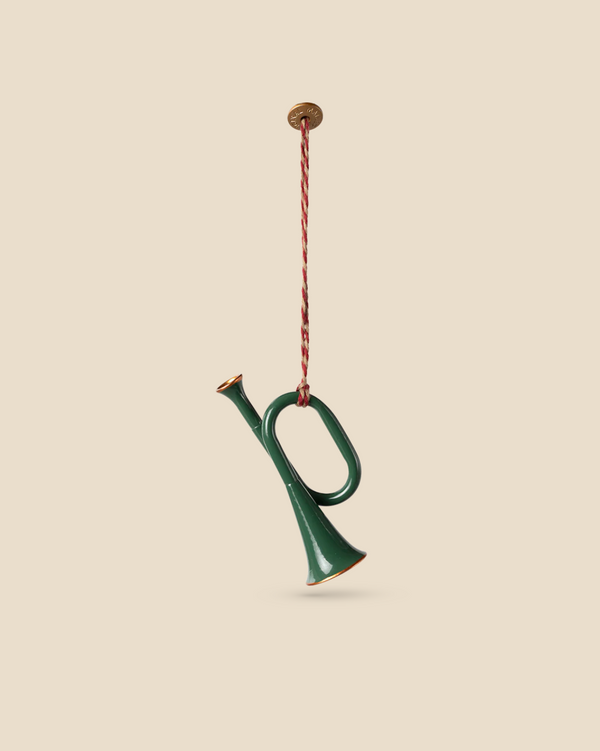 A dark green Maileg Metal ornament, shaped like a trumpet with gold accents, hangs by a red and white twisted rope against a beige background.