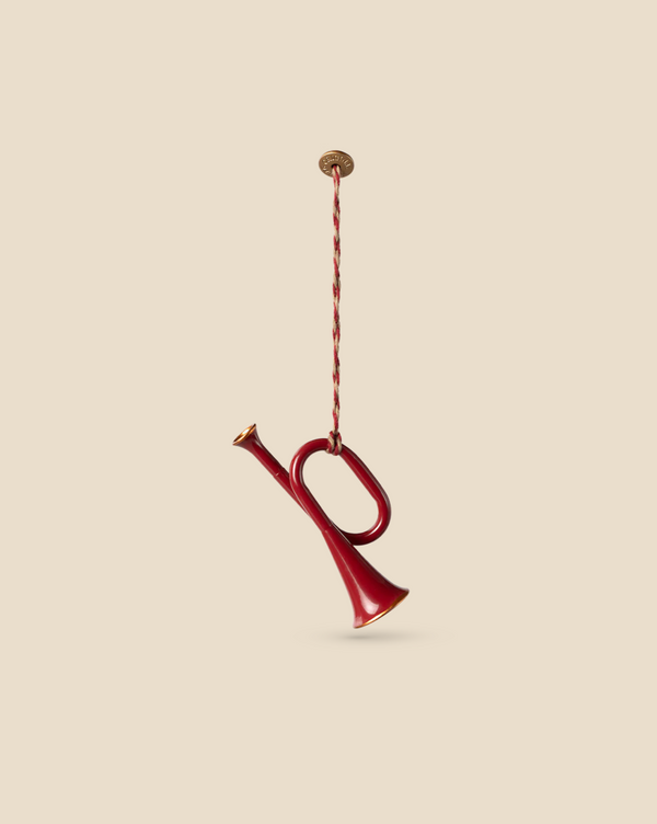 A Maileg Metal Ornament, Trumpet - Red with a brass mouthpiece and handpainted details is suspended by a thin, twisted cord against a plain beige background.