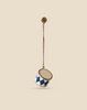 The Maileg Metal Ornament, Small Drum in Dark Blue features blue diamond patterns and hangs elegantly from a red and white twisted cord attached to a brass hook, displayed against a plain beige background.