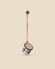 The Maileg Metal Ornament, Small Drum - Classic Red, features handpainted red, white, and blue diamond patterns and hangs from a red and white braided cord attached to a gold-colored hook against a beige background.