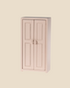 Product Description: The Maileg Mouse Closet - Light Rose is a charming, small wooden wardrobe in a light pink shade. It features two paneled doors, each adorned with a round knob. This minimalist piece, designed to resemble a children's toy, evokes the essence of a tiny mice family closet. Inside, you'll find golden hangers, perfectly complementing the plain beige background.
