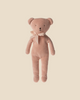 The Maileg Teddy - Rose, featuring a soft and light pink plush cotton fabric, stands upright against a plain beige background. It is adorned with a cream-colored ribbon around its neck and has simple embroidered facial features. Note: This product ships in approximately one week.