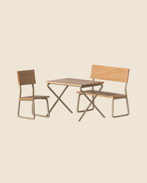 The Maileg Garden Table & Chair Set - Mouse Size is perfect for creating an inviting outdoor space with its minimalist wooden table featuring a metal frame, matching bench with backrest, and chair, set against a neutral backdrop. Ships in approximately one week.