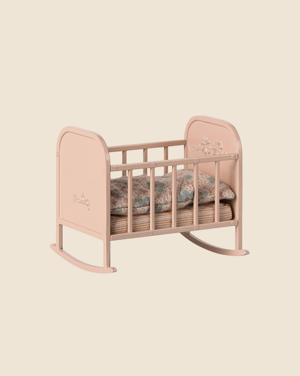 The Maileg My Cradle in Light Rose is a small, pink rocking cradle with floral engravings on the headboard and footboard. It includes a beige mattress and floral-patterned pillow, all on a plain background. Available for pre-order now, it ships late January.