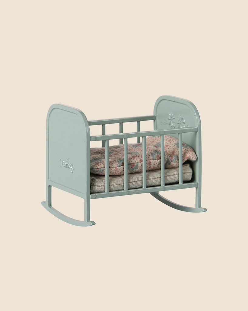 The Maileg My Cradle in Blue Mint features a mini floral-patterned mattress and pillow. Softly rocking to sleep, this small pale green toy crib with floral carvings is available for pre-order and ships in late January, displayed against a beige background.