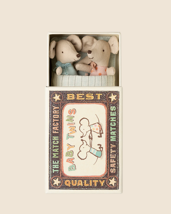 Two twin baby mice in blue and pink outfits snugly fit inside a matchbox bed, labeled as "PRE-ORDER: Maileg Twin Baby Mice In Matchbox (ships late February)." Vintage-style illustrations from Maileg's "The Match Factory" enhance the nostalgia and promise quality.