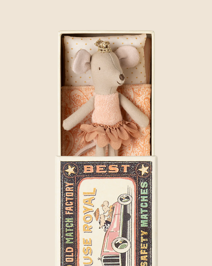 The Maileg Princess Mouse, Little Sister edition, wearing a pink ballerina outfit and gold crown, rests in a uniquely printed miniature matchbox bed with vintage-style artwork. Available for pre-order and shipping in February.