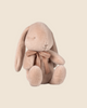 The PRE-ORDER Maileg Plush Bunny in Light Powder, available for shipment in February, is soft and fluffy with a sweet look. It's crafted from recycled polyester, features long ears, wears a brown ribbon around its neck, and sits against a plain beige background.