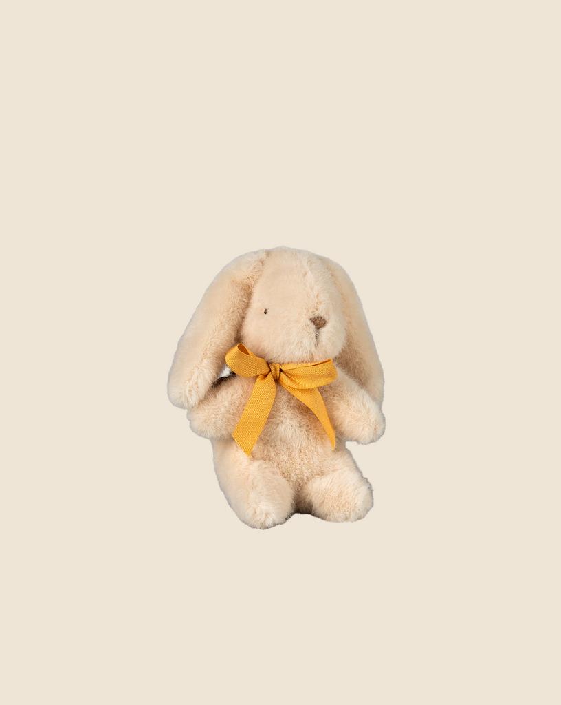 The Maileg Plush Bunny - Mini Cream is a beige toy sitting against a cream background. It features long ears and soft plush made from recycled polyester, complemented by a yellow bow around its neck. Pre-order now for February shipping.