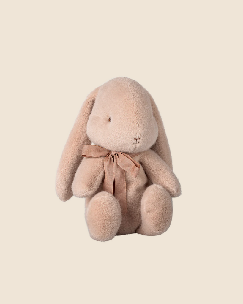 A medium light powder Maileg Plush Bunny with long ears and a brown ribbon sits against a cream background, available for pre-order and shipping in February.