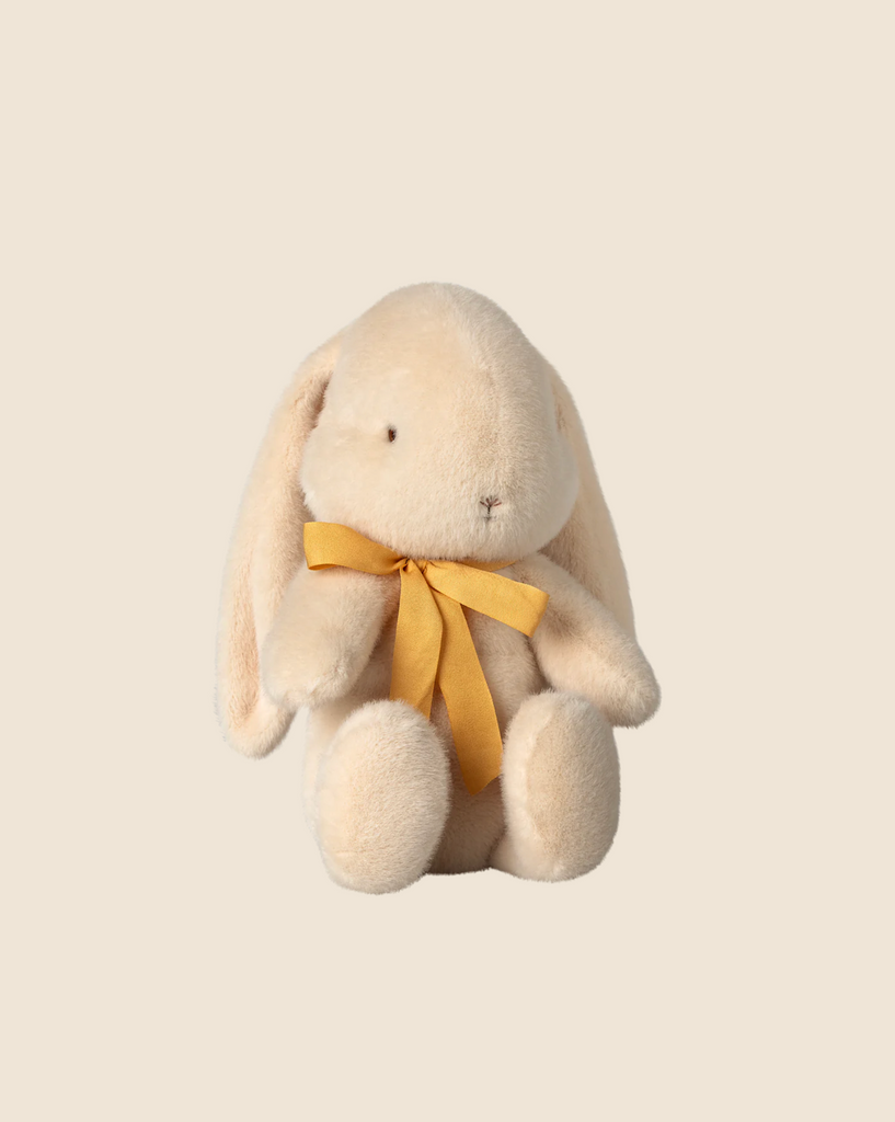 A medium cream Maileg plush bunny, made from recycled polyester with floppy ears and a yellow ribbon, sits against a plain beige background. Available for pre-order now and ships in February.